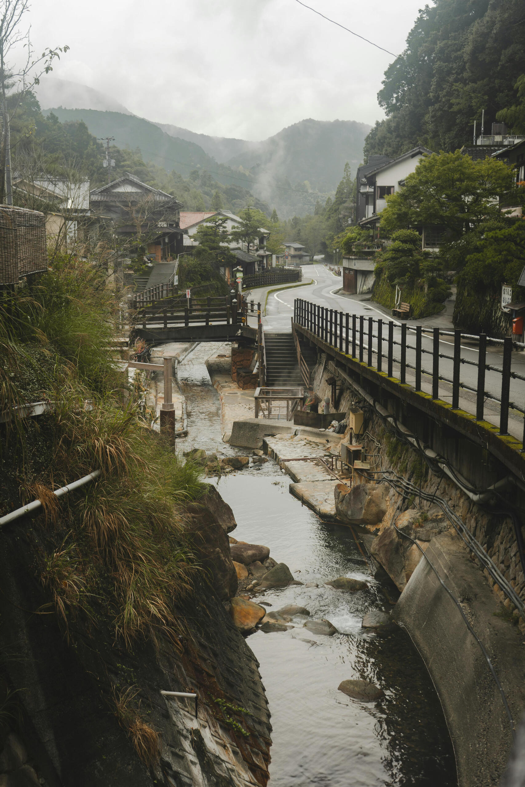 A photo of an overcast, Japanese river with a winding modern street next to it.